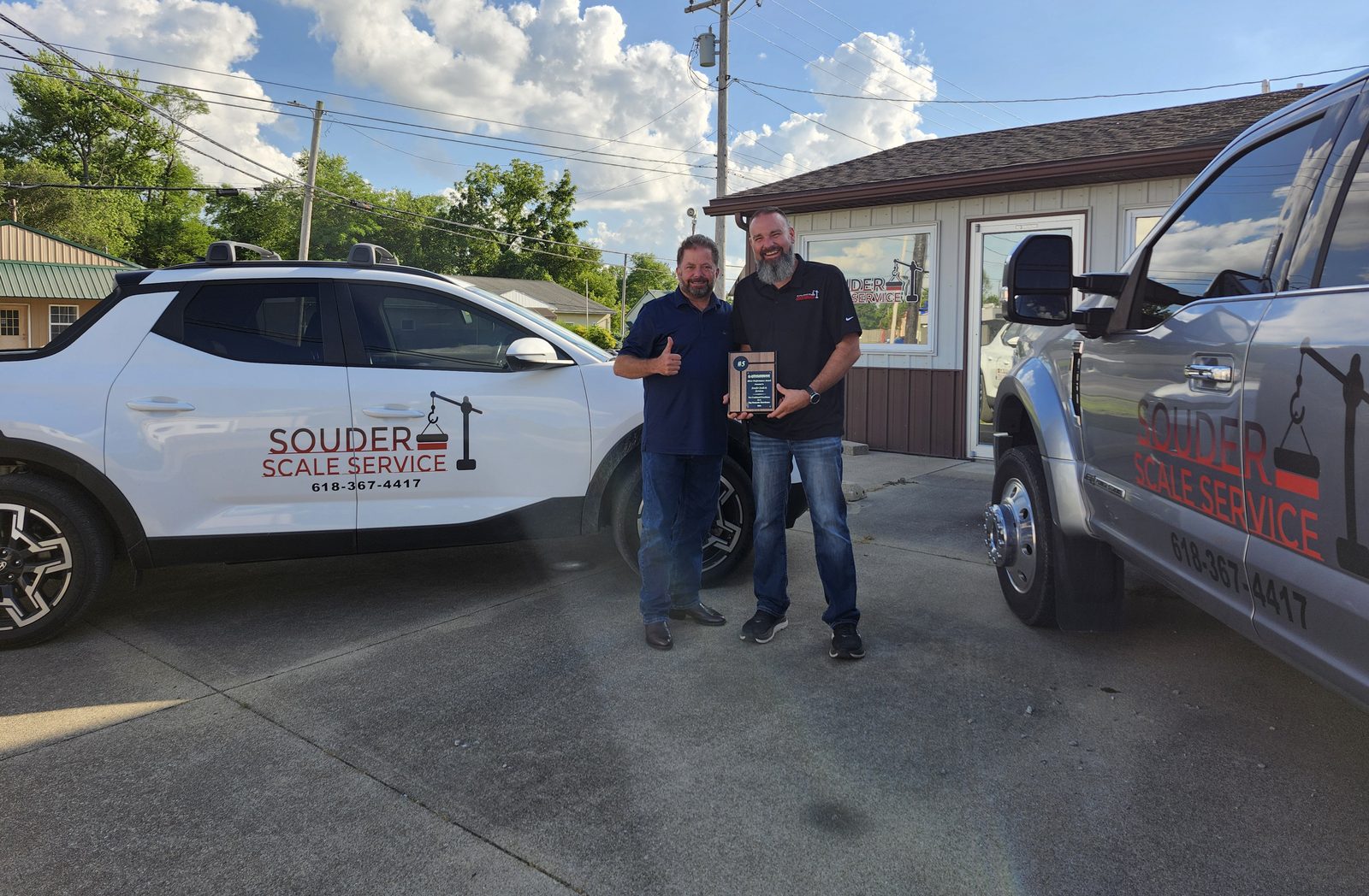 Two people outside the Souder Scale Service office, standing between two service
vehicles lettered with the company name and phone number.