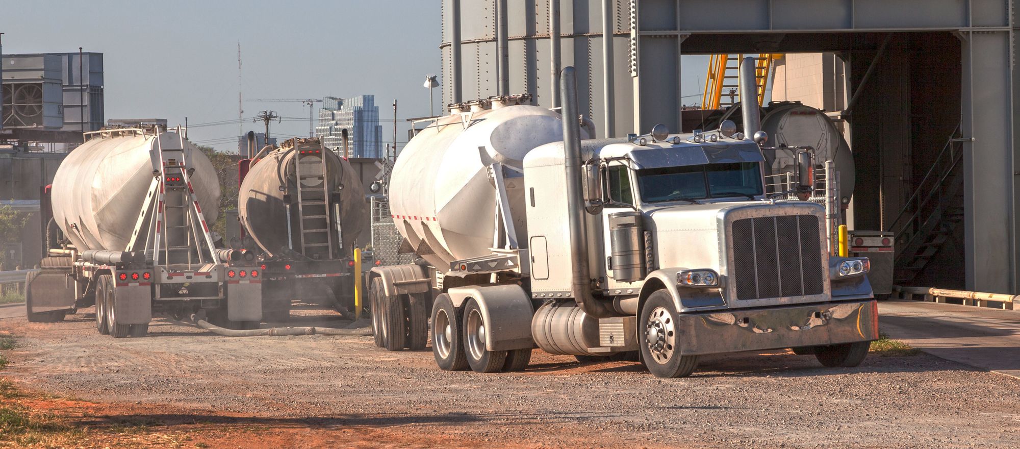 Pneumatic bulk tanker trucks loading under the silo of a cement terminal on a gravel yard